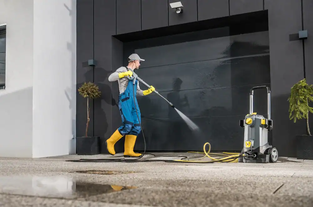 A man wearing yellow rubber boots and blue overalls is power washing a floor—an expert service available in Nassau & Suffolk County, NY.